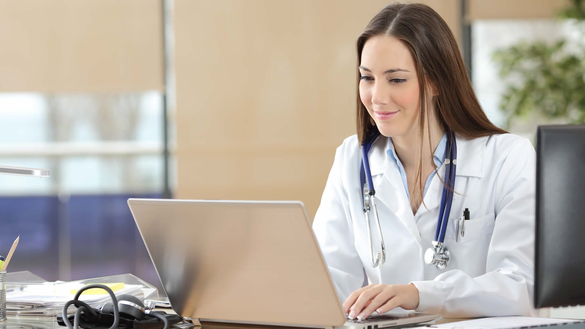 A medical student sits at a desk entering patient information from a visit